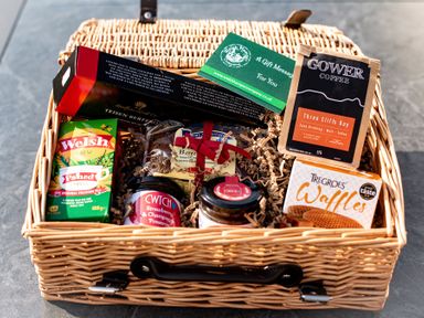 A wicker gift basket containing coffee, tea, waffles, preserves, biscuits, and a gift message card at Swyn Llyr in Rhosneigr