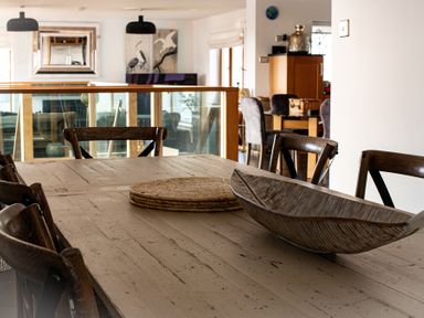 A dining table with wooden chairs and decorative items in a room with glass railing at Swyn Llyr in Rhosneigr