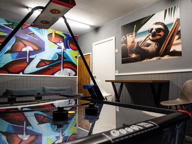 A game room with an air hockey table chairs a table a couch and colorful graffiti art on the wall with a sloth picture at Swyn Llyr in Rhosneigr