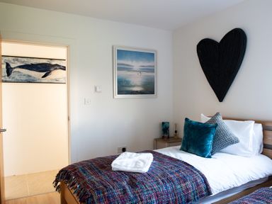A bedroom with a single bed a bedside table and wall art of a heart and seascape at Swyn Llyr in Rhosneigr