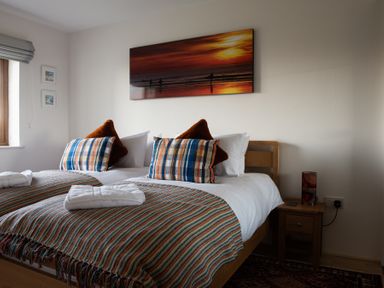 A bedroom with two single beds pushed together with striped blankets and pillows and a wooden nightstand at Swyn Llyr in Rhosneigr