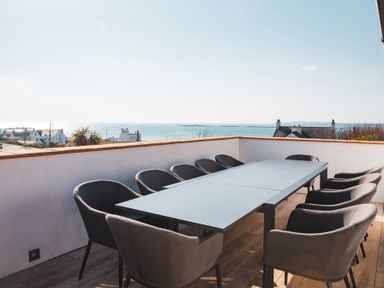 An outdoor patio with a rectangular table and chairs overlooking the sea at Swyn Llyr in Rhosneigr