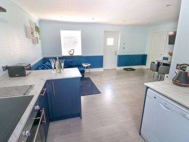 A kitchen and dining area with blue cabinets a corner sofa and a small dining table at Bluebell Cottage in St Brides-super-Ely near Cardiff