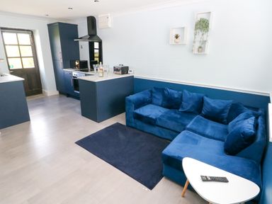 A kitchen with blue cabinets and a blue sofa with cushions and a small white table with a remote at Bluebell Cottage in St Brides-super-Ely near Cardiff