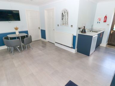 A kitchen area with a small dining table and chairs a wall-mounted TV and a kitchenette unit at Bluebell Cottage in St Brides-super-Ely near Cardiff