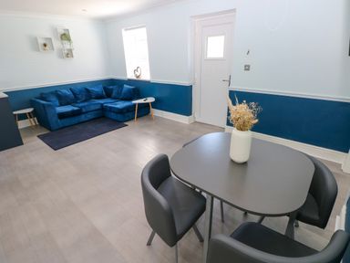 A dining area with four chairs and a table with a vase of flowers and a living area with a blue sofa and side tables at Bluebell Cottage in St Brides-super-Ely near Cardiff