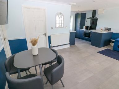 A dining area with a table and four chairs next to a kitchen with dark cabinets and appliances at Bluebell Cottage in St Brides-super-Ely near Cardiff