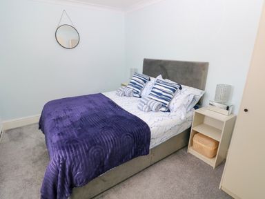 A bedroom with a double bed blue blanket pillows bedside tables and a round wall mirror at Bluebell Cottage in St Brides-super-Ely near Cardiff