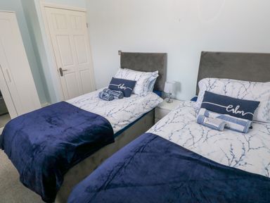 A bedroom with two single beds with blue and white bedding and a small white bedside table with a lamp at Bluebell Cottage in St Brides-super-Ely near Cardiff