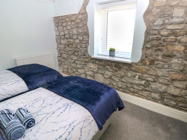 A bedroom with a stone wall, a window with blinds, a bed with blue and white bedding, and rolled towels at Bluebell Cottage in St Brides-super-Ely near Cardiff