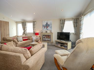 A living room with beige sofas a television fireplace and a rocking chair at 21 Norman Drive Lodge in Burgh Castle