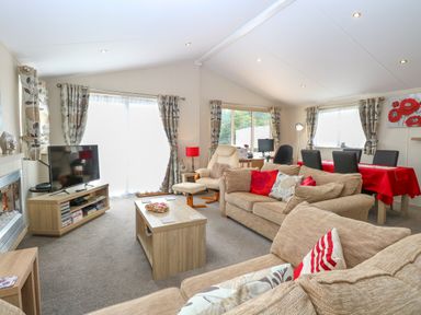 A living room with beige sofas a wooden coffee table a television and a dining table with red tablecloth at 21 Norman Drive Lodge in Burgh Castle