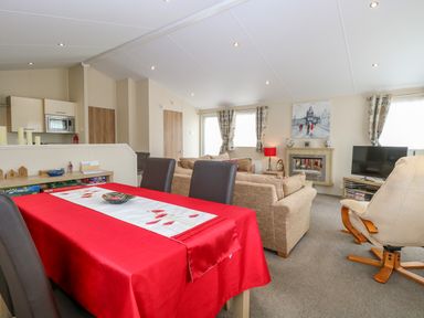 A living room and dining area with a red tablecloth on the table beige sofas a television and a fireplace at 21 Norman Drive Lodge in Burgh Castle