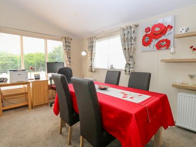 A dining room with a red tablecloth on a table and four black chairs at 21 Norman Drive Lodge in Burgh Castle