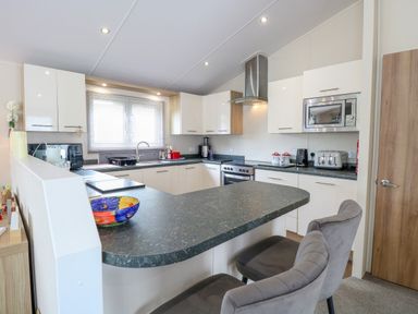 A kitchen with white cabinets grey countertop stainless steel appliances and two grey chairs at 21 Norman Drive Lodge in Burgh Castle