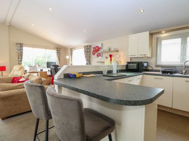 An open plan kitchen and living area with chairs at a countertop and a sofa at 21 Norman Drive Lodge in Burgh Castle