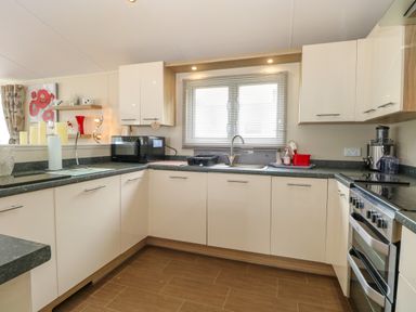 A kitchen with white cabinets black countertops a window with blinds a microwave and an oven at 21 Norman Drive Lodge in Burgh Castle
