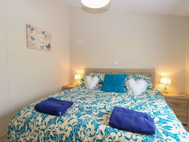 A bedroom with a double bed with patterned bedding and two bedside tables with lamps at 21 Norman Drive Lodge in Burgh Castle