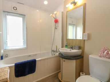 A bathroom with a bathtub shower combination a sink with a mirror and a toilet at 21 Norman Drive Lodge Burgh Castle