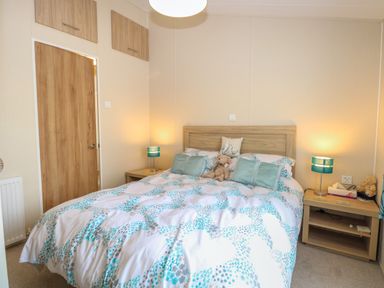 A bedroom with a double bed covered in patterned bedding with teddy bears and two bedside tables with lamps at 21 Norman Drive Lodge in Burgh Castle