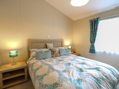 A bedroom with a double bed two bedside tables with lamps and a window with curtains at 21 Norman Drive Lodge in Burgh Castle