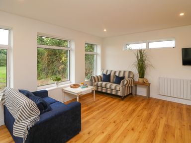 A living room with two sofas a coffee table a side table with a plant and windows showing greenery outside at The Farm Cottage in Athy County Kildare
