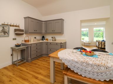 A kitchen with grey cabinets a small table with bowls a wooden dining table with a lace tablecloth and chairs at The Farm Cottage in Athy County Kildare