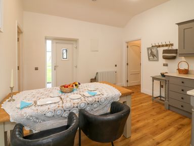 A dining area with a wooden table covered by a lace tablecloth two black chairs and kitchen cabinets at The Farm Cottage in Athy County Kildare