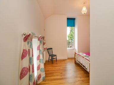 A bedroom with wooden floor a window with blue blind a single bed a black chair and curtains with red and blue leaf patterns at The Farm Cottage in Athy County Kildare
