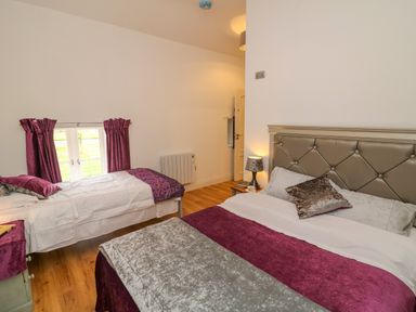 A bedroom with two beds a lamp on a bedside table and purple curtains at The Farm Cottage in Athy County Kildare