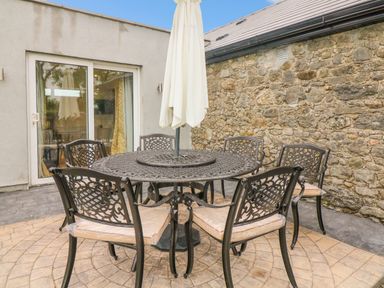 An outdoor patio area with a round metal table and six matching chairs with cushions and a closed umbrella at The Farm Cottage in Athy County Kildare
