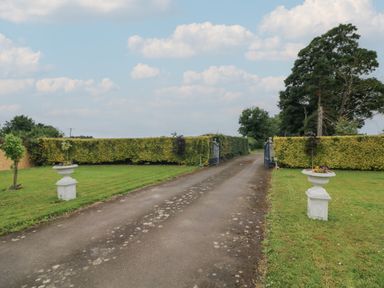 A paved driveway with two open metal gates lined with hedges and stone planters at The Farm Cottage in Athy County Kildare
