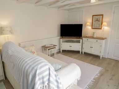 A living room with a sofa a television on a cabinet and two table lamps at Ty Hafan in Mostyn