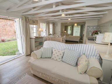 An open living space with a sofa and cushions a dining table and chairs a bed kitchen appliances and an open door leading to a garden at Ty Hafan in Mostyn