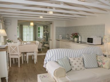 A living area with a sofa and cushions a dining table with chairs and a kitchen with appliances at Ty Hafan in Mostyn