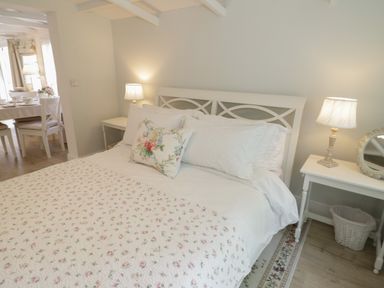 A bedroom with a bed with floral bedding two bedside tables with lamps and a view of a dining area at Ty Hafan in Mostyn