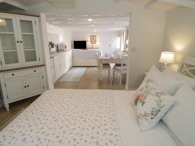 A bedroom with a bed and floral bedding leading to a dining area and kitchen with white cabinets and furniture at Ty Hafan in Mostyn