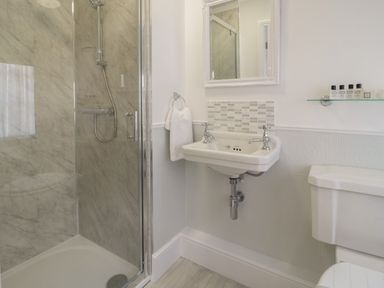 A bathroom with a shower cubicle a white sink a mirror a toilet and toiletries on a glass shelf at Ty Hafan in Mostyn