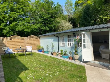 A garden with lawn chairs and table near a light blue shed with potted plants along the side at Ty Hafan in Mostyn