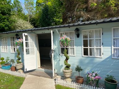 A light blue garden shed with white double doors open and potted plants along the front at Ty Hafan in Mostyn