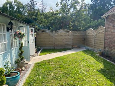 A garden with grass and a path bordered by plants and a light blue wooden shed with hanging flower baskets and adjacent brick wall at Ty Hafan in Mostyn