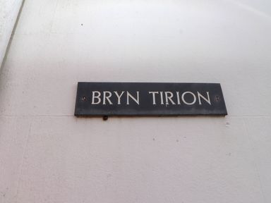 A black sign with white letters saying Bryn Tirion mounted on a white wall at Bryn Tirion in Morfa Nefyn