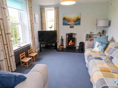A living room with a fireplace a television two sofas and two small wooden chairs at Bryn Tirion in Morfa Nefyn