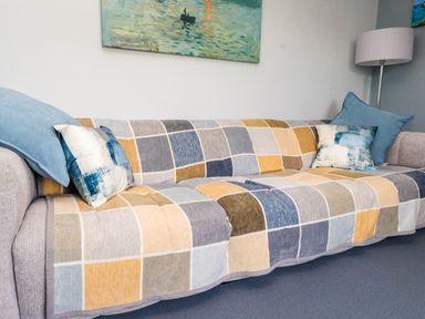 A sofa with a checkered blanket and cushions with a lamp and painting in the background at Bryn Tirion in Morfa Nefyn