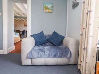 A small armchair with two blue cushions and a blue throw in a room with light blue walls and a doorway leading to a dining area at Bryn Tirion in Morfa Nefyn
