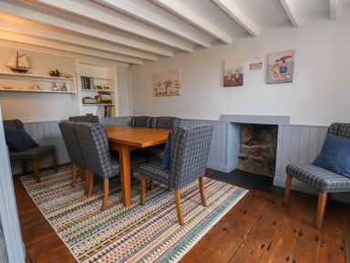 A dining room with wooden table and six checkered chairs a fireplace and built in bookcase at Bryn Tirion in Morfa Nefyn