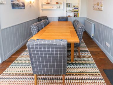 A dining room with a wooden table surrounded by grey checkered chairs and bookshelves at Bryn Tirion in Morfa Nefyn