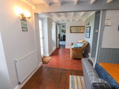 A hallway with a wicker chair with cushions a tiled floor and a door leading to another room at Bryn Tirion in Morfa Nefyn