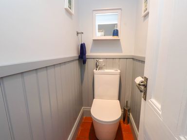 A small bathroom with a toilet a blue towel a mirror and a soap dispenser at Bryn Tirion in Morfa Nefyn