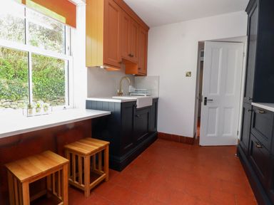 A kitchen with black and orange cabinets wooden stools and a window with a view of greenery at Bryn Tirion in Morfa Nefyn